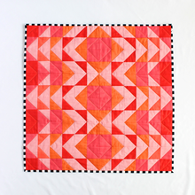 Load image into Gallery viewer, Quilt with a geometric triangle pattern in red, orange, and pink on a white background