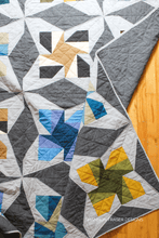 Load image into Gallery viewer, Quilt with star patterns in gray, blue, green, and yellow on a wooden surface.