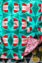 Load image into Gallery viewer, Quilt with geometric pattern featuring red, white, and teal colors, with a folded corner showing a different fabric.