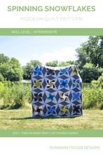 Load image into Gallery viewer, Bring winter charm to your sewing room with the Spinning Snowflakes quilt pattern! Inspired by snowflakes and built with snowball blocks and HRTs, this modern quilt is perfect for holiday decor or cozy seasonal gifting. Includes baby, lap, double &amp; queen sizes. #WinterQuilt #SnowflakeQuilt #HolidayQuilting #ModernQuiltPattern