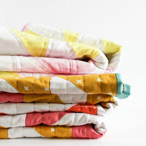Pretty stack of bright colorful quilts featuring. Make your own today with the easy Pink Lemonade quilt pattern. #modernquilting #konacotton #quiltpattern