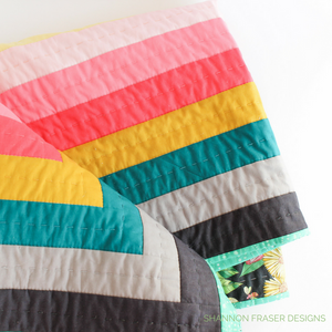 Rainbow quilt featuring modern log cabin quilt design using the Reveberance Quilt Pattern designed by Shannon Fraser Designs